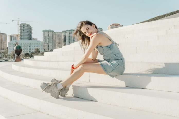 Young woman in denim dress sitting on white steps