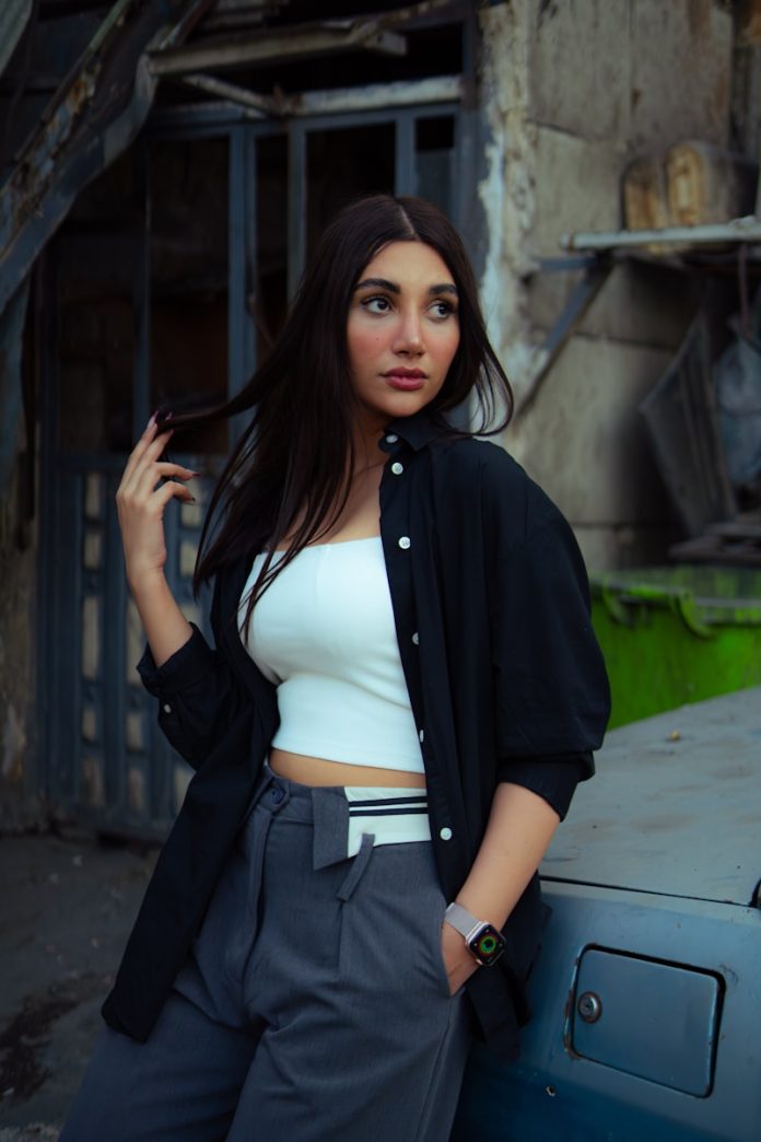 A young woman in stylish clothes leans against a car.
